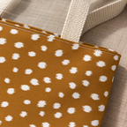 Close-up of the white fawn spots on caramel brown and the cream handle of the tote bag