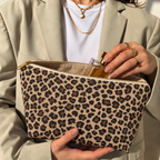 Woman opening the brown leopard print makeup bag to take out a perfume bottle