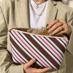 Hands holding the open brown pink diagonal striped makeup bag