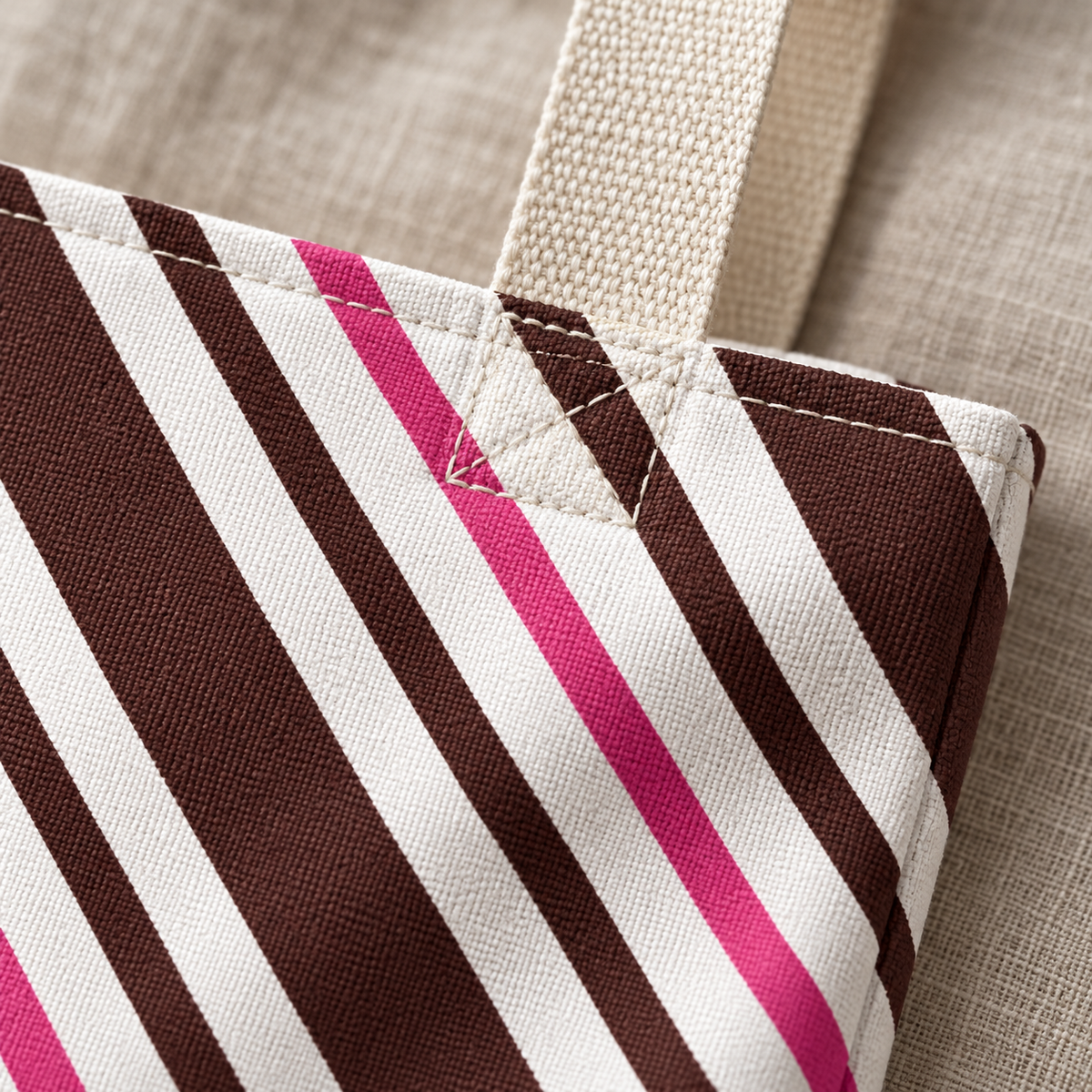 Close-up of the brown, pink and white diagonal stripes and the beige handle on the brown pink diagonal striped tote bag