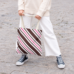 Woman in white trousers holding the brown pink diagonal striped tote bag by its handles