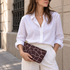 Woman holding a giraffe print makeup bag in brown and pink like a clutch