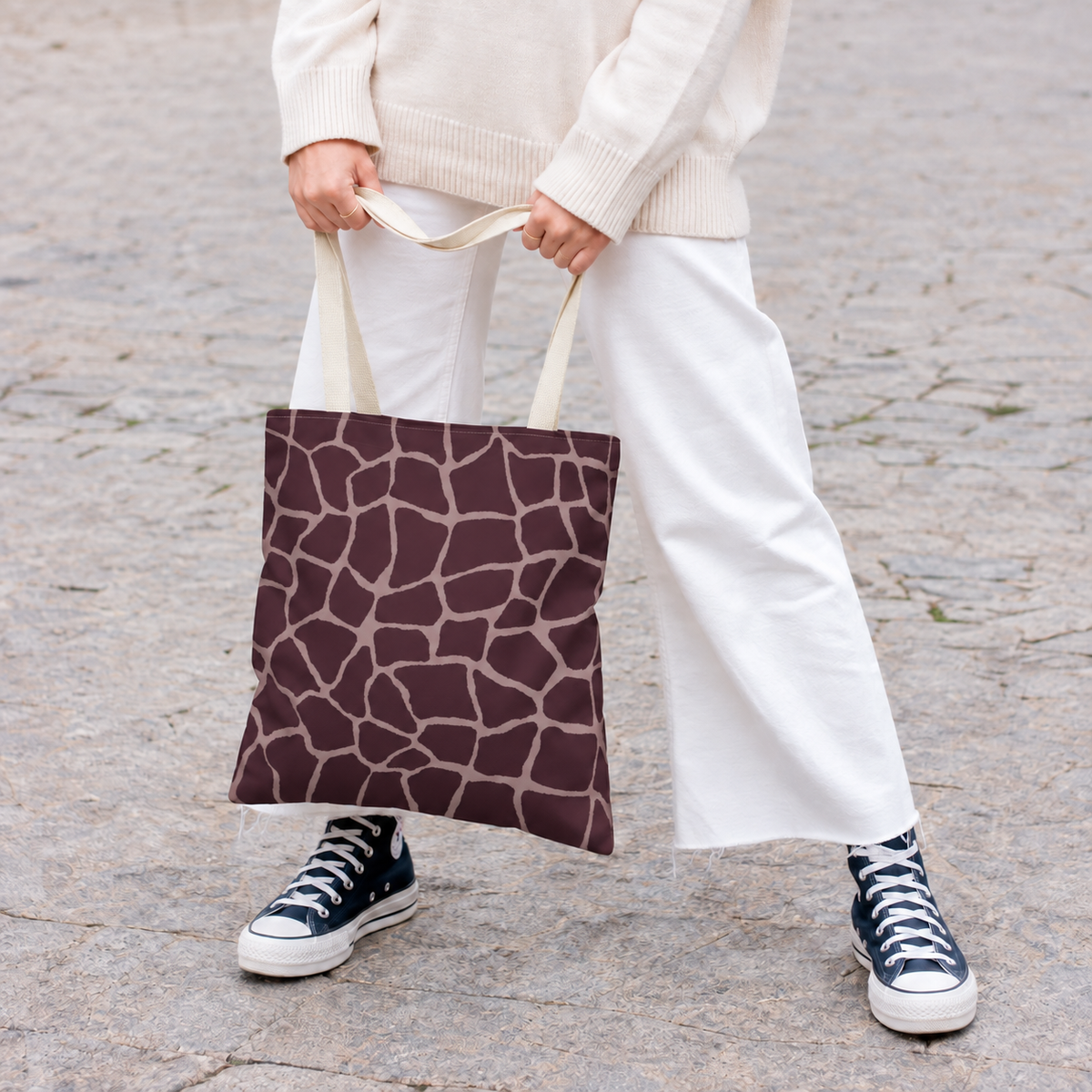 Woman holding a brown pink giraffe print tote bag with white trousers and sneakers