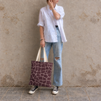 Woman leaning on a wall with a giraffe print tote bag in brown and pink