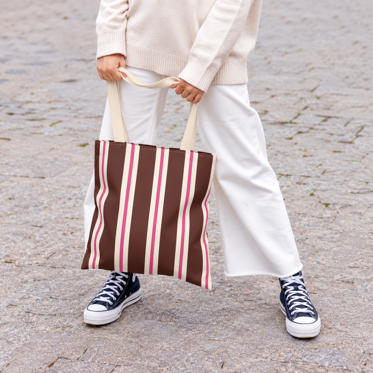 Woman in white trousers holding the brown pink striped tote bag by its handles