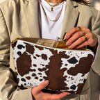 Hands opening a brown white cow print makeup bag filled with cosmetics