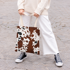 Woman holding a brown white cow print tote bag with white trousers and sneakers