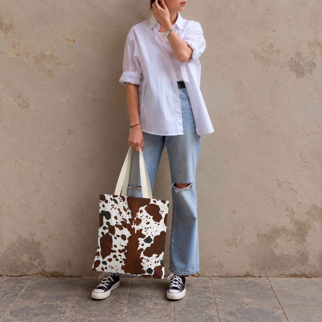 Woman leaning on a wall holding a brown white cow print tote bag