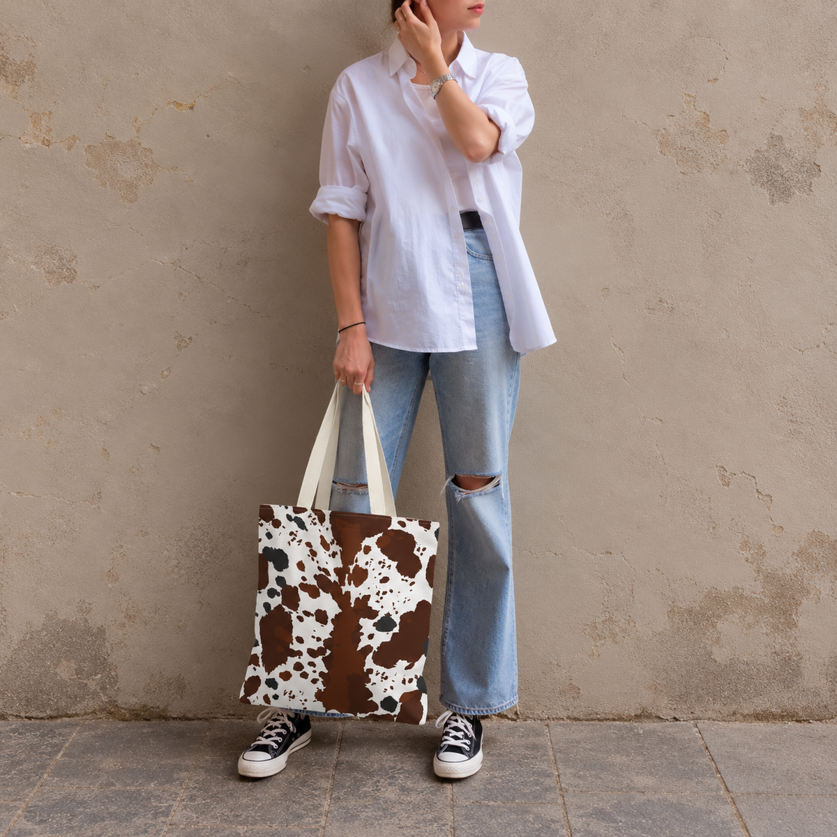 Woman leaning on a wall holding a brown white cow print tote bag