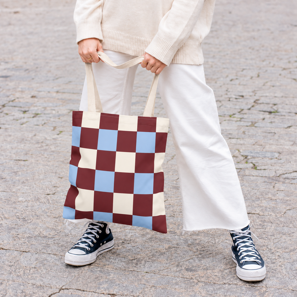 Woman in white trousers holding the burgundy blue cream checkered tote bag by its handles