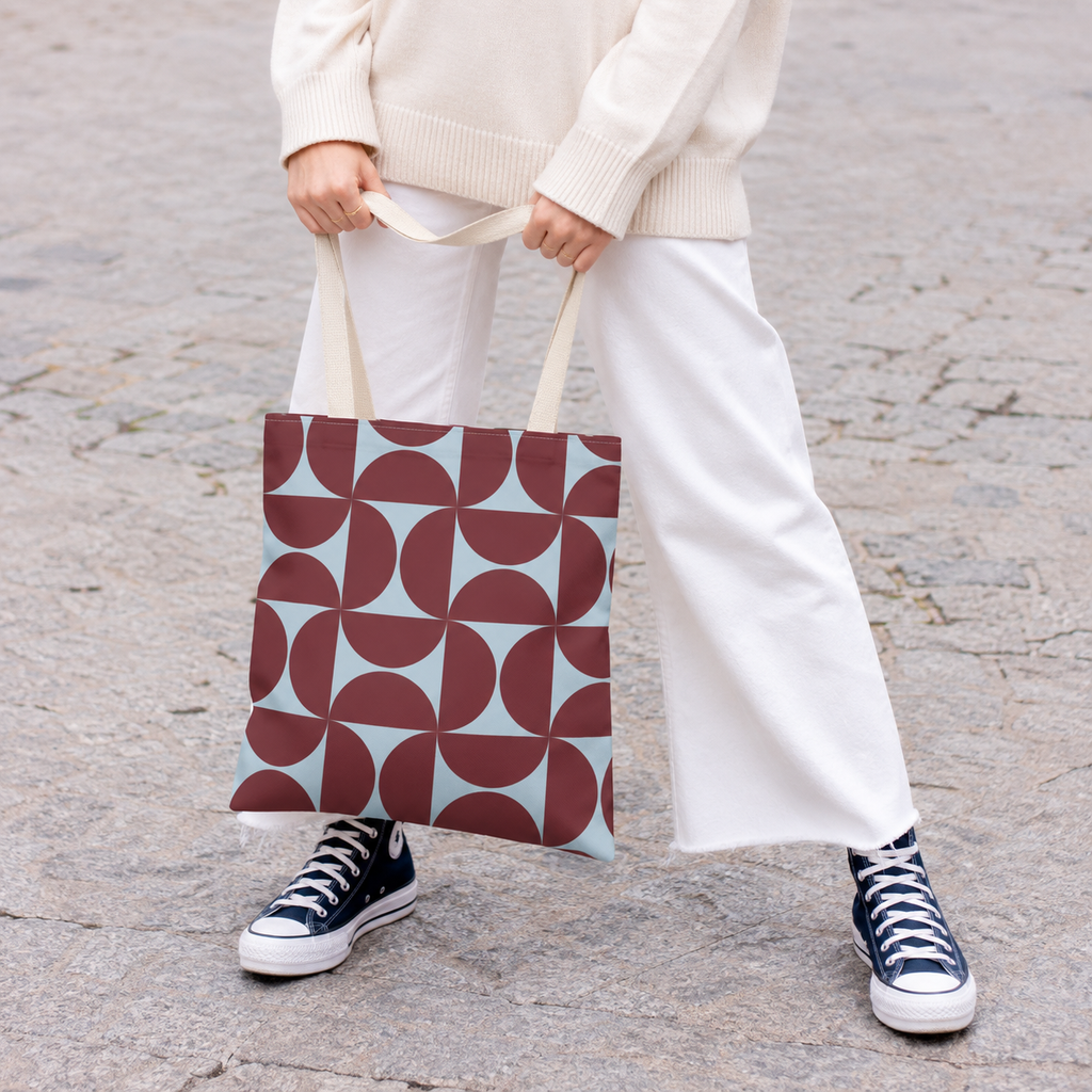 Woman in white trousers holding the burgundy blue geometric tote bag by the handles