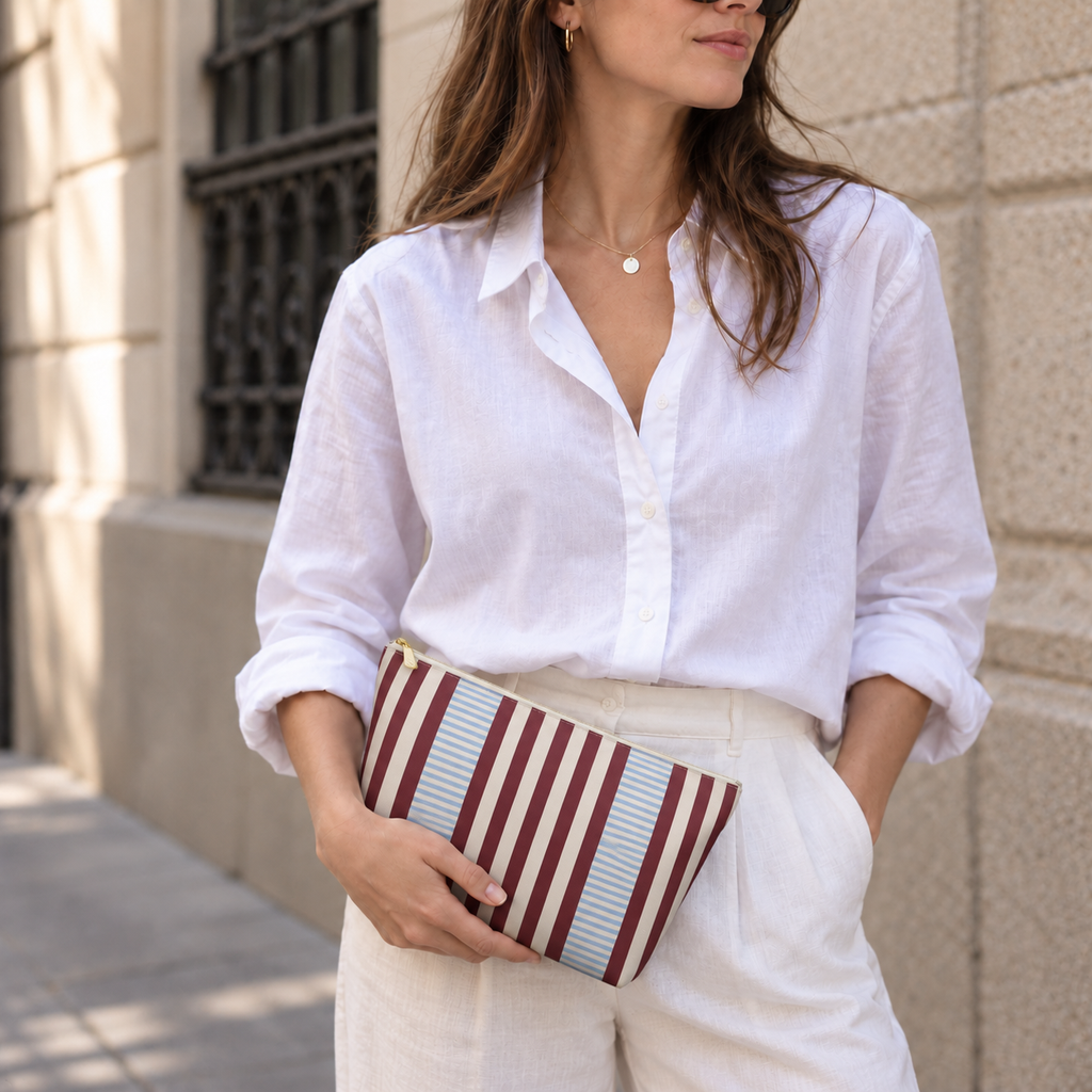 Woman in a white shirt holding the burgundy blue pinstripe makeup bag as a clutch
