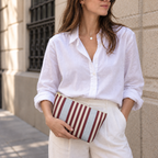 Woman in a white shirt holding the burgundy blue pinstripe makeup bag as a clutch