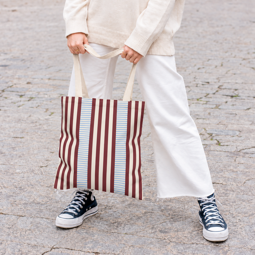Woman in white trousers holding the burgundy blue pinstripe tote bag by its handles