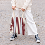 Woman in white trousers holding the burgundy blue pinstripe tote bag by its handles