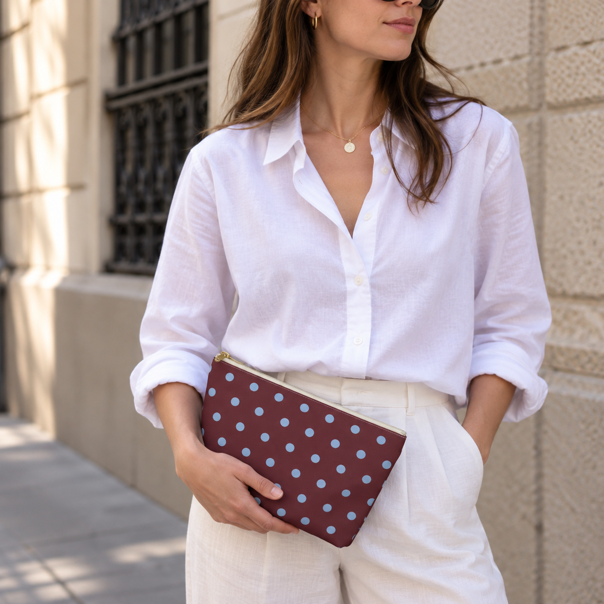 Woman in a white shirt holding the burgundy polka dot makeup bag at her hip