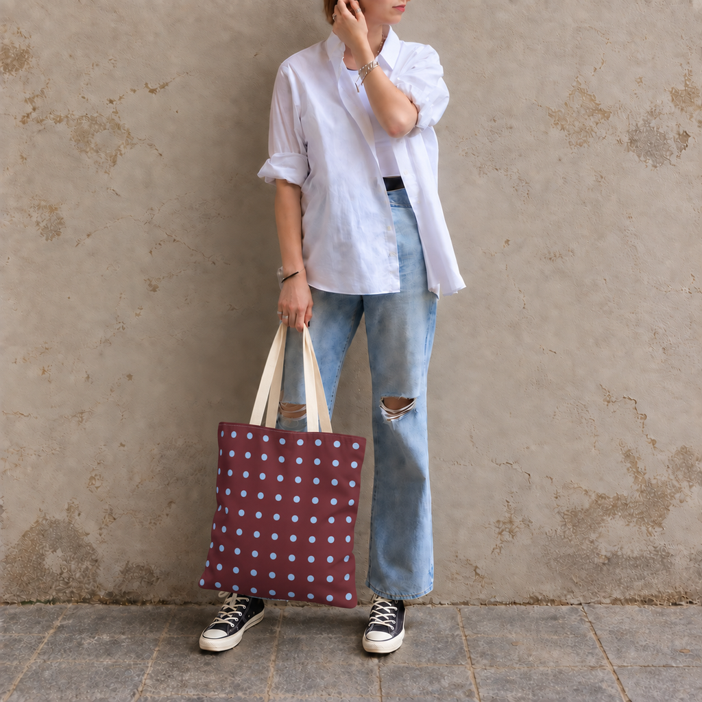 Woman in a light shirt and jeans holding the burgundy blue polka dot tote bag against a wall