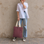 Woman in a light shirt and jeans holding the burgundy blue polka dot tote bag against a wall