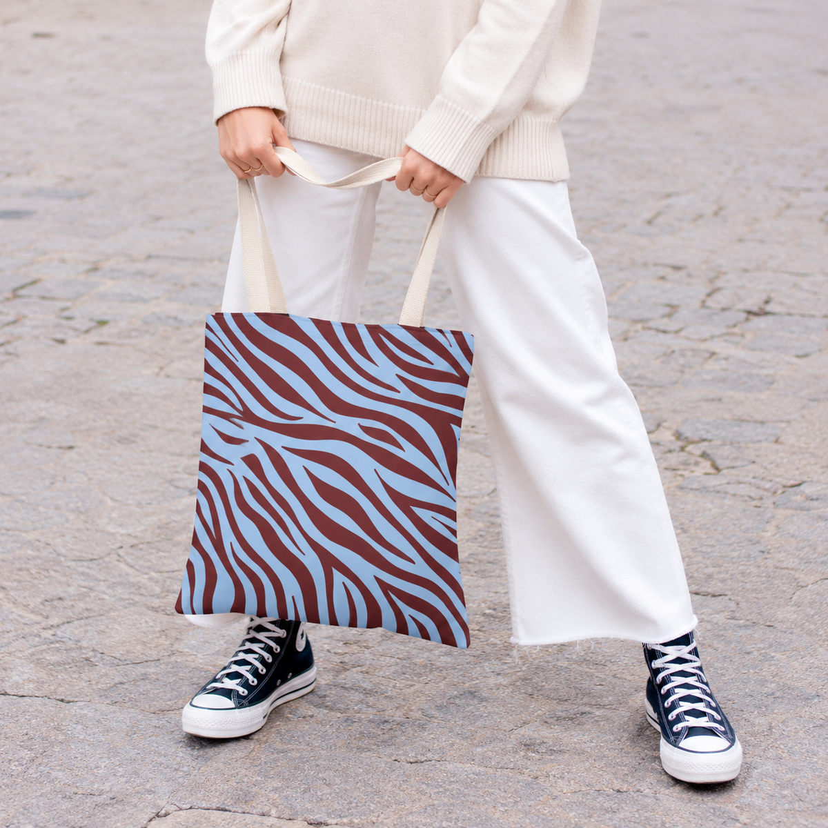 Woman holding the burgundy blue zebra print tote bag in front of her on a street