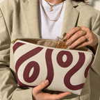 Hands holding the open burgundy cream abstract makeup bag