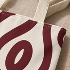 Close-up of the burgundy abstract loop print on cream and the beige handle of the tote bag