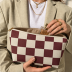Hands holding the open burgundy cream checkered makeup bag