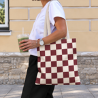 Side view of a person carrying the burgundy cream checkered tote bag on the shoulder