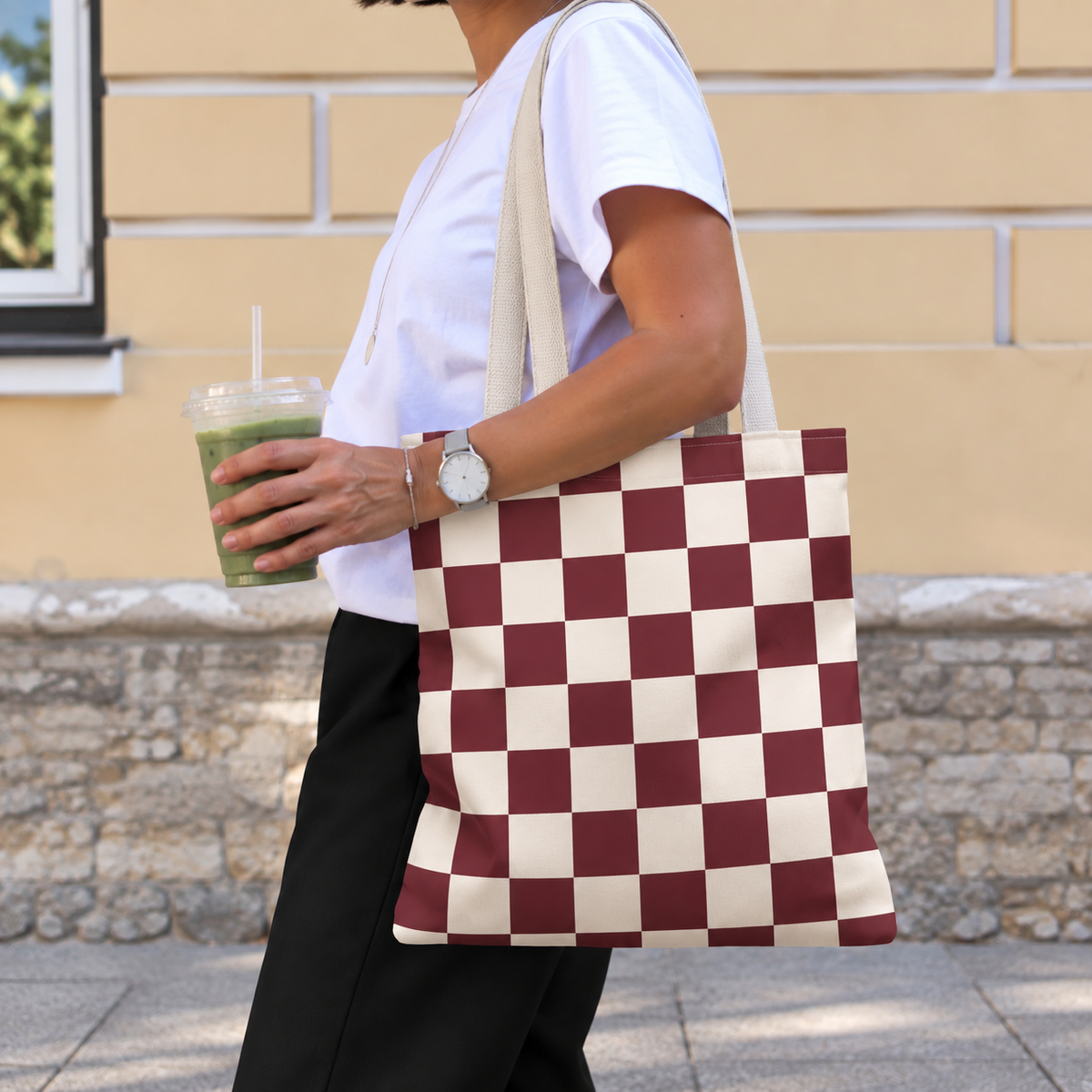 Side view of a person carrying the burgundy cream checkered tote bag on the shoulder