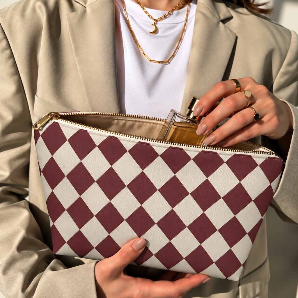 Hands opening a burgundy cream diamond checkered makeup bag filled with cosmetics