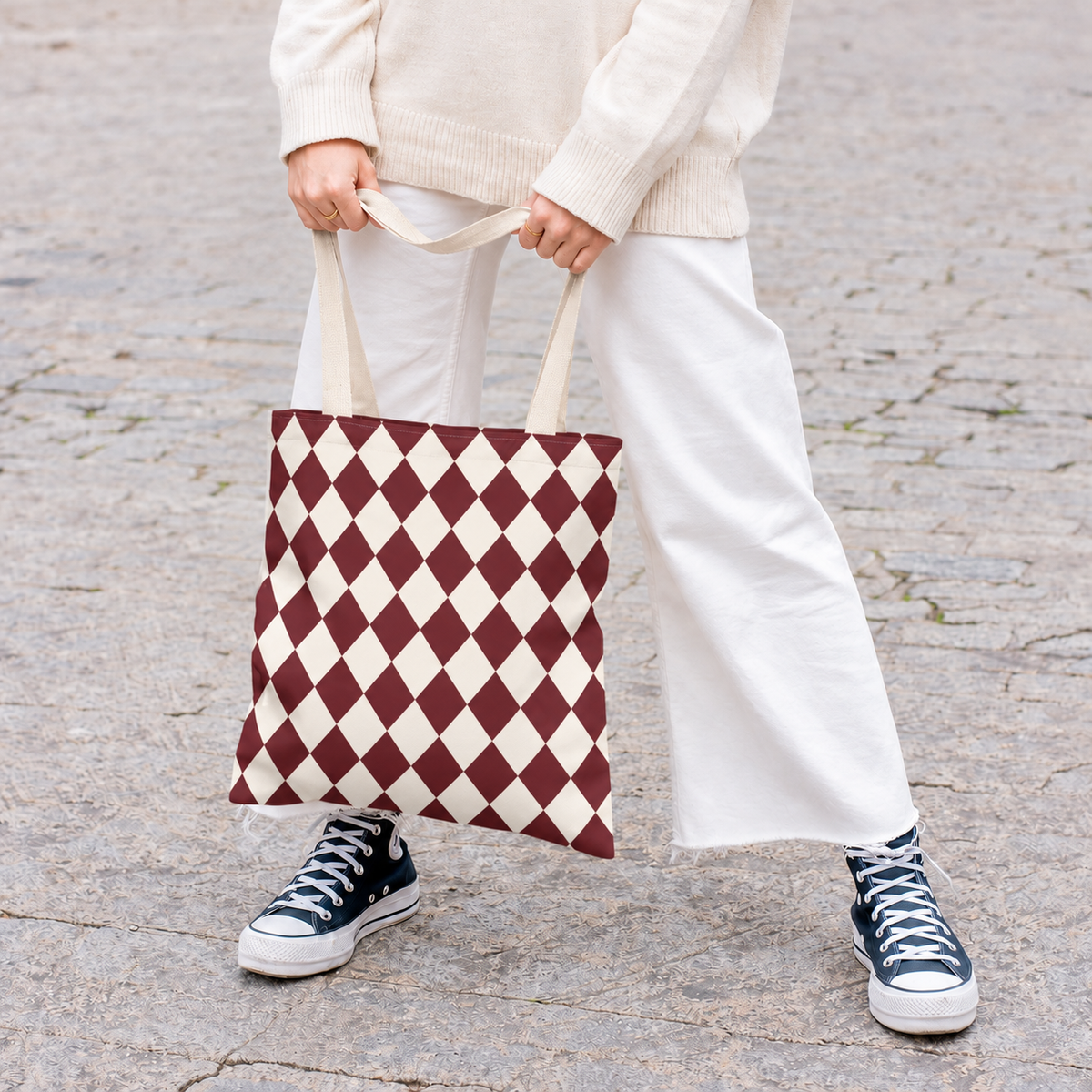 Woman holding a burgundy diamond checkered tote bag with white trousers and sneakers
