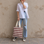 Woman leaning on a wall with a burgundy cream diamond checkered tote bag