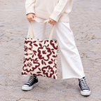 Woman in white trousers holding the burgundy cream floral tote bag by the handles