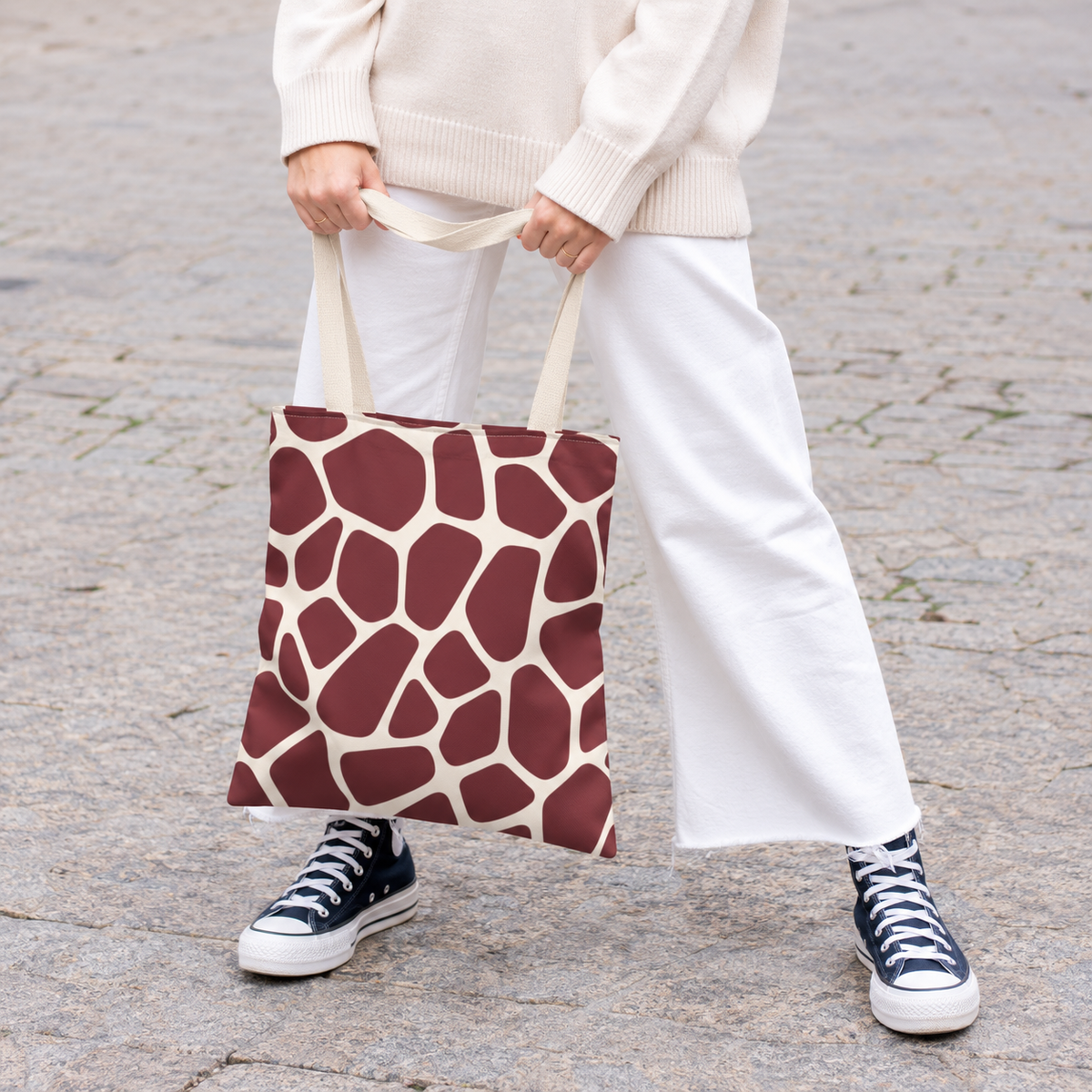 Woman holding a burgundy giraffe print tote bag with white trousers and sneakers