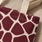Close-up of burgundy giraffe patches with cream lines and the tote bag handle