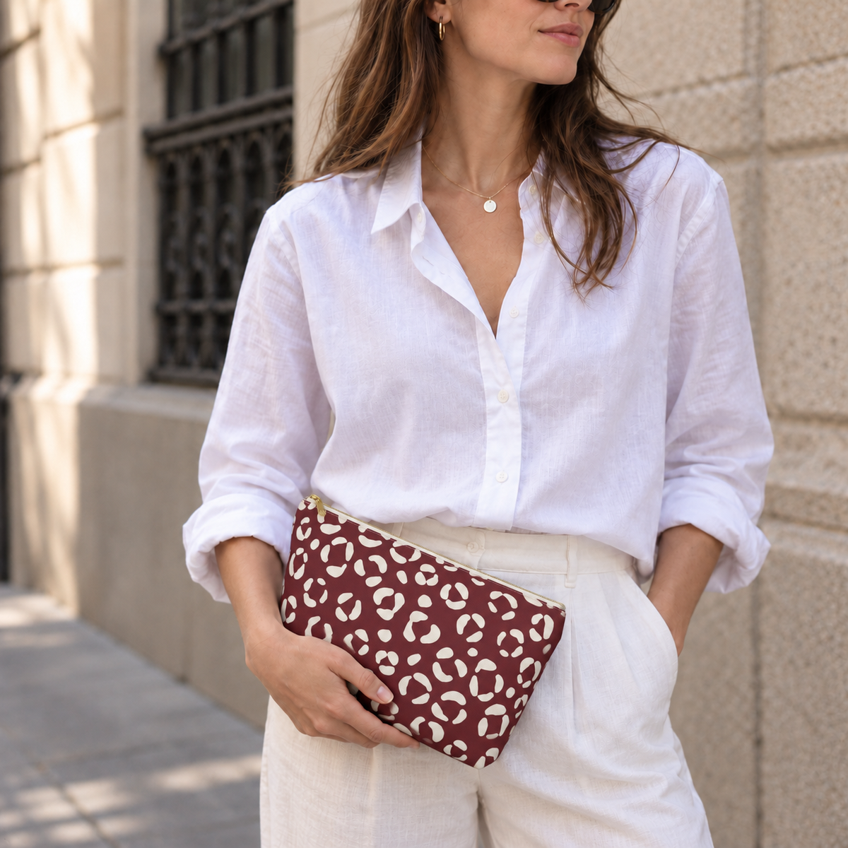 Woman in a white blouse holding a burgundy cream leopard print makeup bag