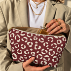 Hands opening a burgundy leopard print makeup bag filled with cosmetics
