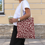 Woman with a burgundy tote bag covered in cream leopard spots over her shoulder