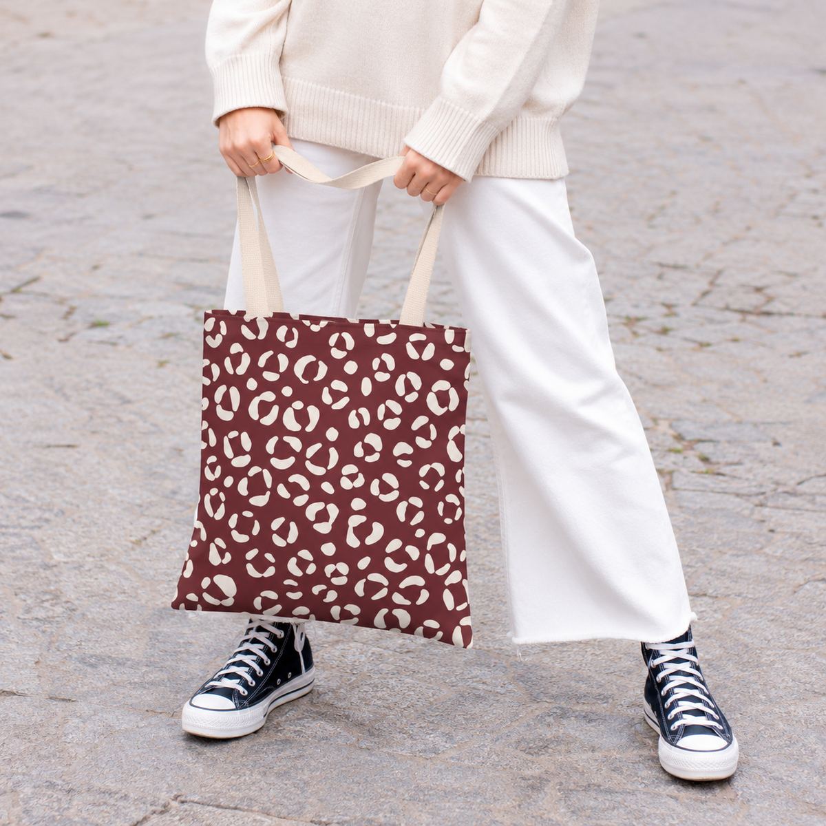 Woman holding a burgundy leopard print tote bag with white trousers and sneakers
