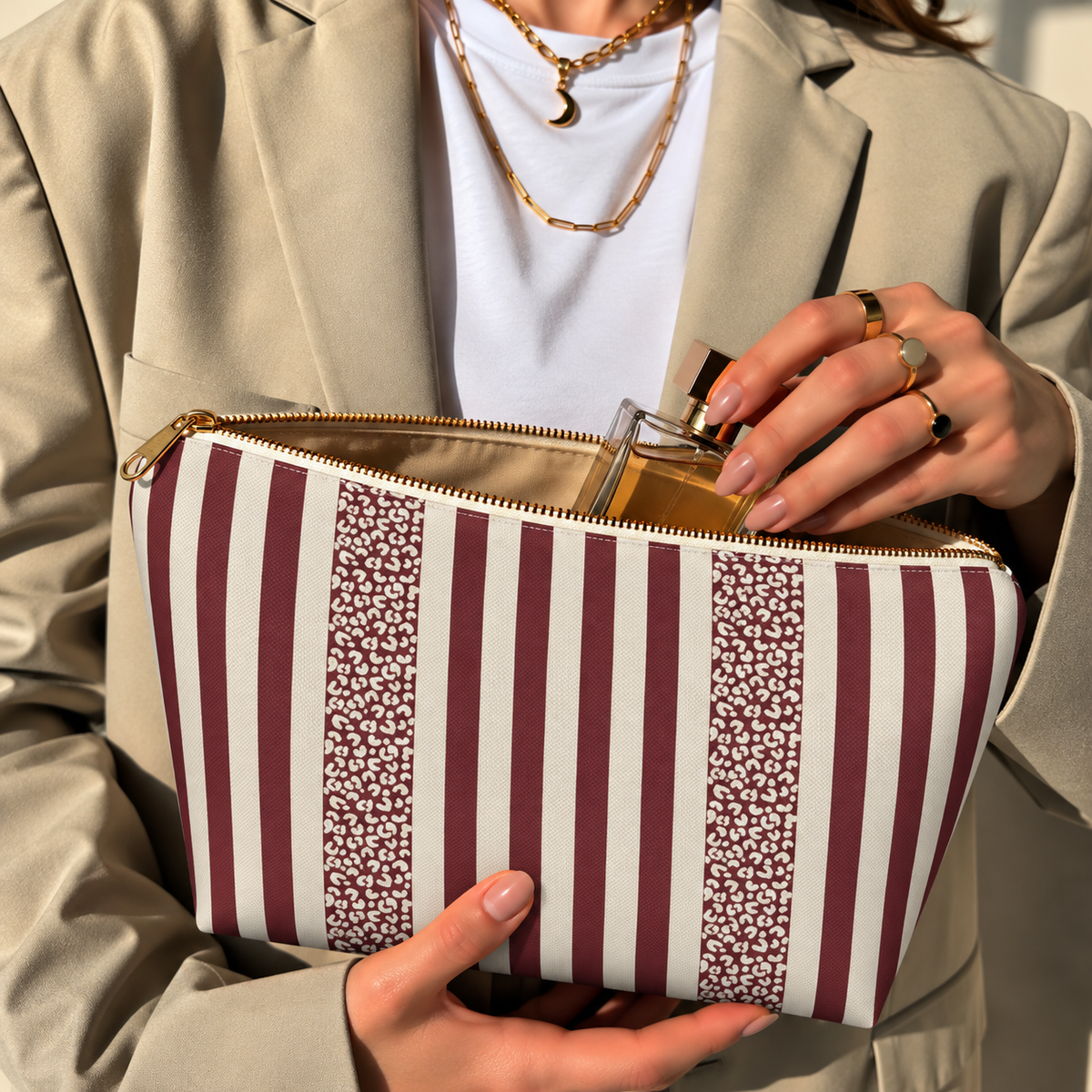 Hands opening a burgundy cream striped makeup bag filled with cosmetics