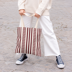 Woman holding a burgundy cream striped tote bag with white trousers and sneakers