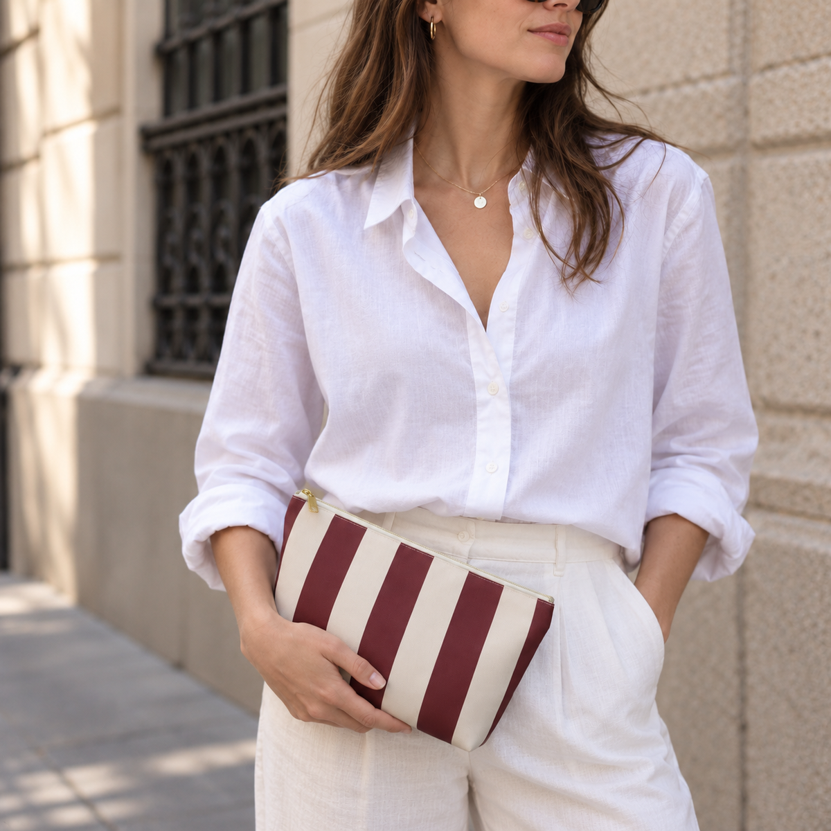 Woman in a white shirt holding the burgundy cream striped makeup bag as a clutch