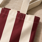 Close-up of the wide burgundy and cream stripes and the beige handle on the burgundy cream striped tote bag