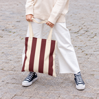 Woman in white trousers holding the burgundy cream striped tote bag by its handles