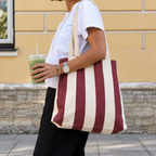Woman carrying the burgundy cream striped tote bag on her shoulder on the street