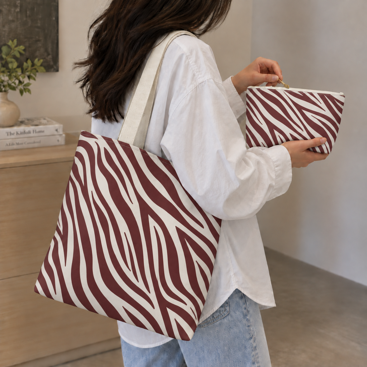 Model carrying the zebra print tote bag while holding the matching burgundy makeup bag