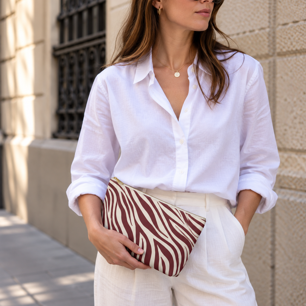 Woman in a white shirt holding the burgundy zebra print makeup bag at her hip
