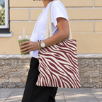 Side view of a woman carrying the burgundy cream zebra print tote bag on her shoulder