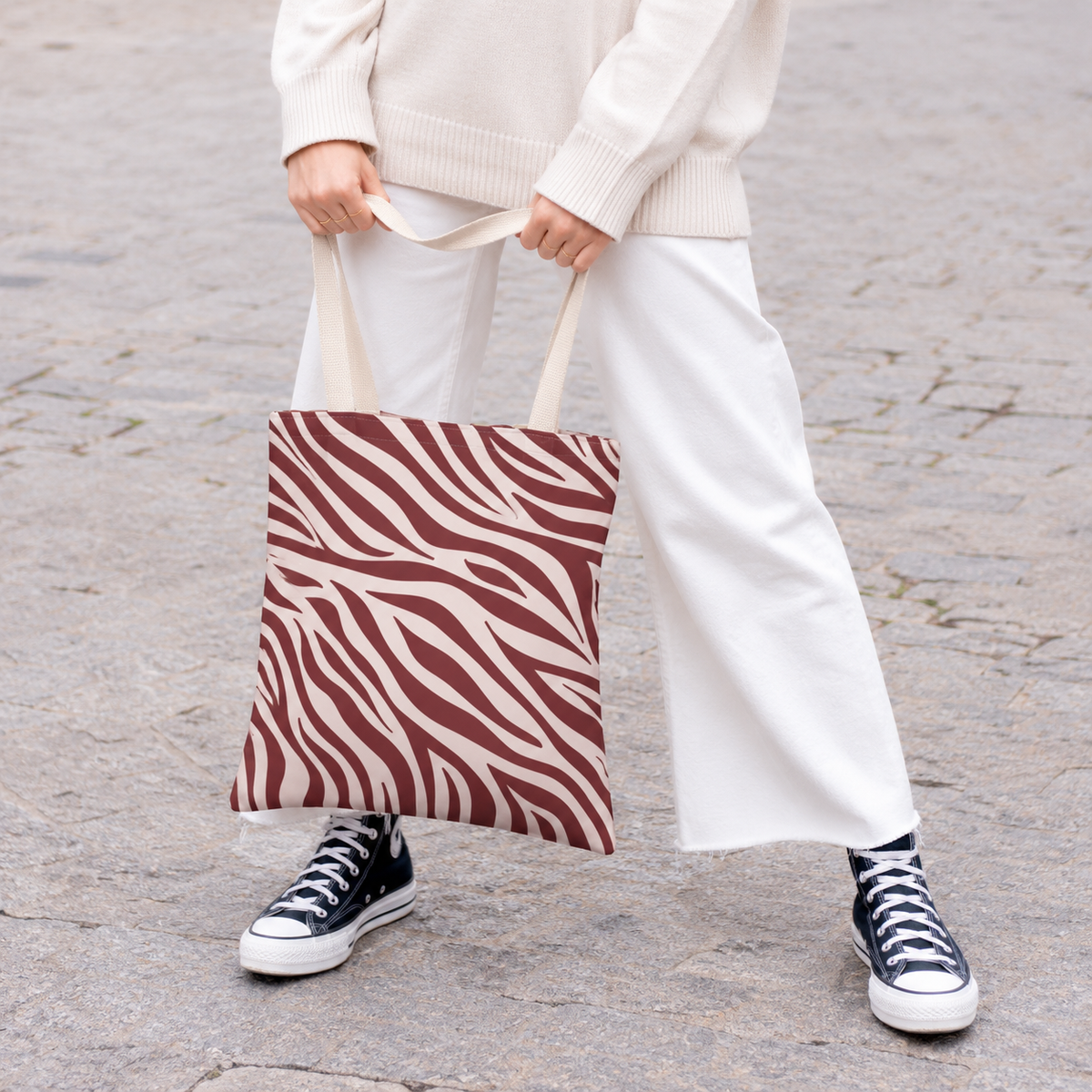 Woman in light trousers holding the burgundy cream zebra print tote bag in front of her