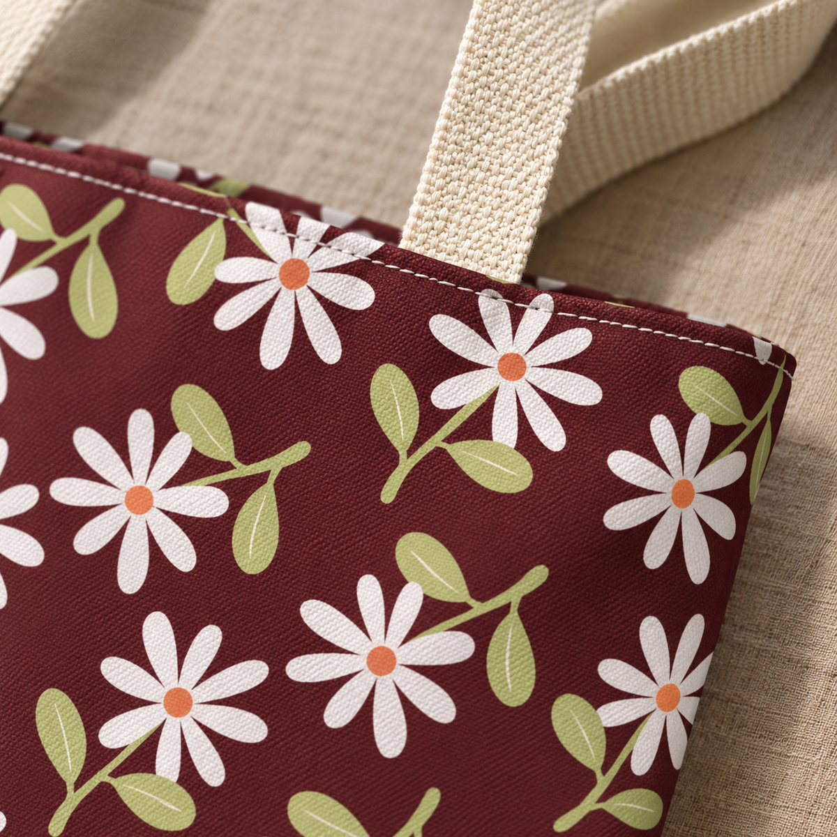 Close-up of white daisies and green leaves on burgundy next to the tote handle