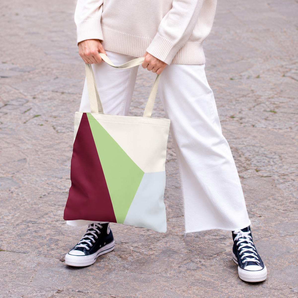 Model in white trousers holding the burgundy green color block tote bag